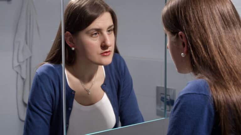 sad woman looking in mirror, why women stay in abusive relationships