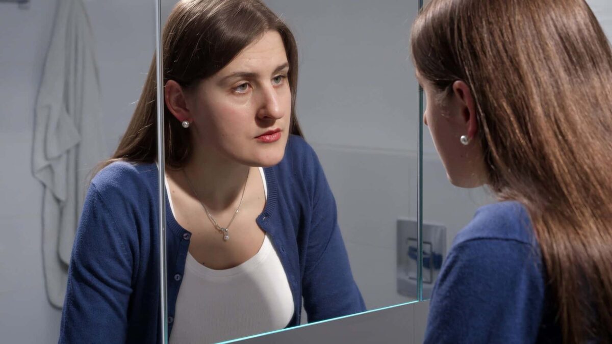 sad woman looking in mirror, why women stay in abusive relationships